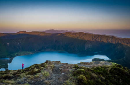 Woman traveller standing on the rim and taking pictures of the stunningly beautiful volcanic crater lake Lagoa do Fogo ( Fire Lake ), Sao Miguel, Azores, Portugal.の写真素材