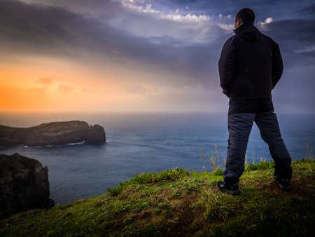 Traveller standing on the top of a cliff and admiring the sunset, Sao Miguel Island in the Azores, Portugalの写真素材