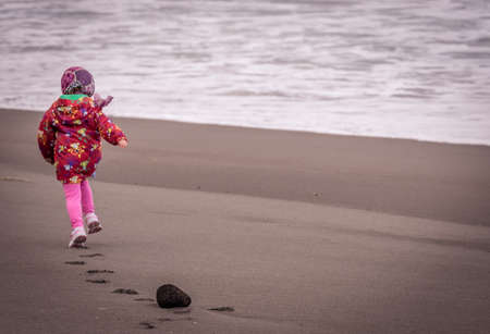 Little girl running on the beach on the coast in Sao Miguel, Azores, Portugalの写真素材