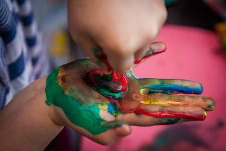 Child extracting more paint from the tube on his or her hand, already dirty from many colorsの写真素材