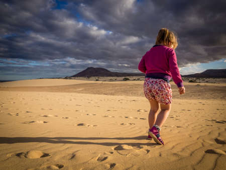 Little girl walking on the sand on the sand dunes in  the Natural Reserve of Dunes in Corralejo, Fuerteventura, Canary Islands, Spainの写真素材