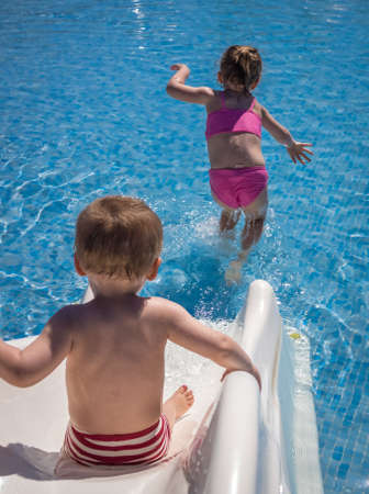Cute two years old boy and four years old girl having fun on the small water slide in the outdoor swimming poolの写真素材
