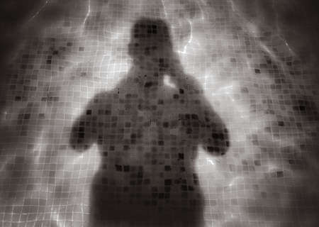 Silhouette reflection of a man in a water of a swimming pool with squared pattern floor tilesの写真素材