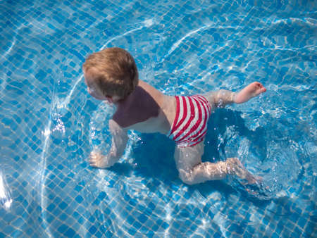 Cute two years old boy attempting to swim on his own for the first time in the outdoor swimming pool in a holiday resortのeditorial素材
