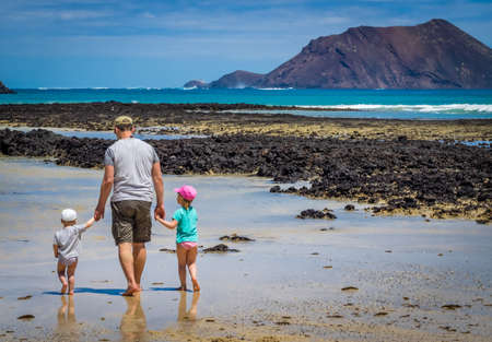 Father with his children, little boy and girl, walking in water waiting for wave to come on the beach in summerのeditorial素材