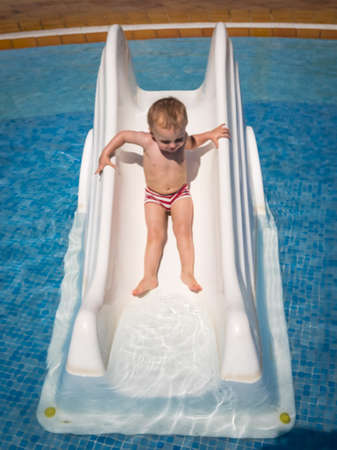 Cute two years old boy having fun on the small water slide in the outdoor swimming poolのeditorial素材