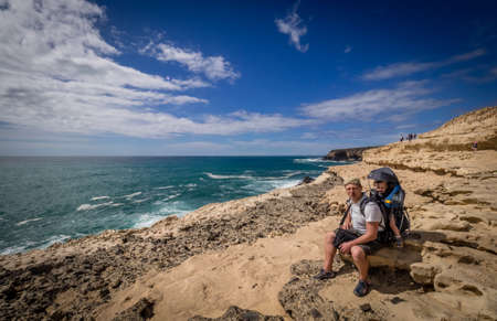 Father resting with his son in a child carrier while trekking along the coastline in Ajuy, Parque Rural de Betancuria in Fuerteventura, Canary Island, Spain. Picture taken 13 April 2016のeditorial素材
