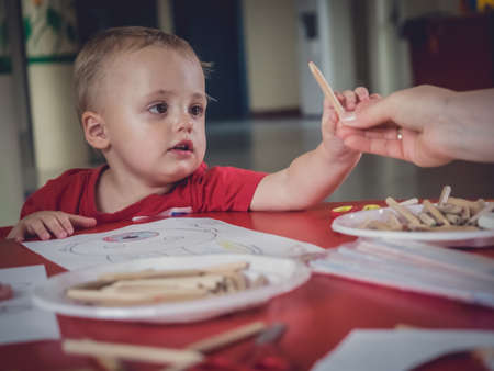 Woman passing a crayon to the little boy during art time activities at the nurseryの写真素材