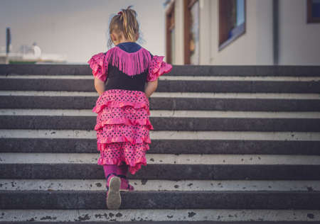 Little four years old girl dressed in pink salsa costume  going up the stairs in townの写真素材