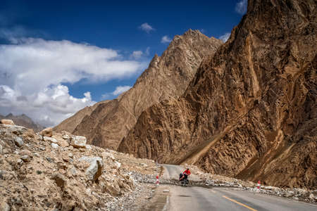Solo female cyclist crossing the mountain stream on the remote road in Xinjang province leading to Western Tibetの写真素材
