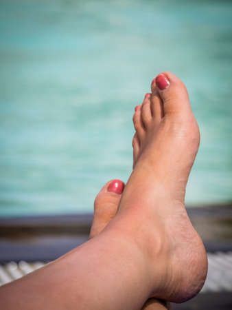 Closeup of feet of a woman sunbathing at deckchair by the swimming pool in a holiday resort