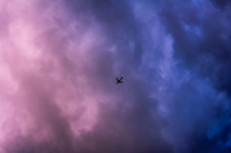 Commercial passenger plane flying over the dark stormy blue evening skyの写真素材