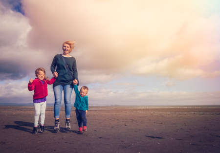 Mom with her daughter and son jumping up in the air together on a beachの写真素材