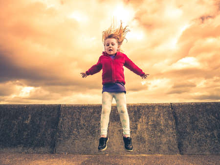 Little girl jumping from the concrete wall on the seaside promenadeの写真素材