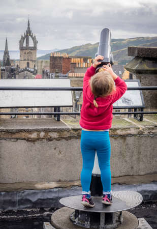 Little girl stretching to to be able to look through the telescope on the viewing platform on top of Camera Obscura in Edinburgh, Scotlandの写真素材