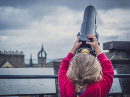 Little girl stretching to to be able to look through the telescope on the viewing platform on top of Camera Obscura in Edinburgh, Scotlandの写真素材