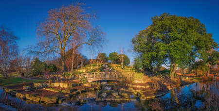 London, England - December 29, 2016: Panoramic picture of a couple on the wooden bridge in front of a small artificial waterfall in Regents Park, Londonのeditorial素材