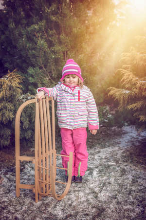Portrait of a little girl standing in a park and holding her wooden sledの写真素材