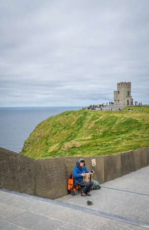 Cliffs of Moher, Ireland -  April 2017 : Musician with an accordion sitting on the footpath leading to the O`Briens Tower at the Cliffs of Moher, Irelandのeditorial素材