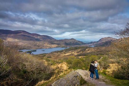 Killarney National Park, Ireland -  April 2017 : Couple of tourists standing on a large rock and taking pictures of the mountains and lakes in the Killarney National Park, Irelandのeditorial素材