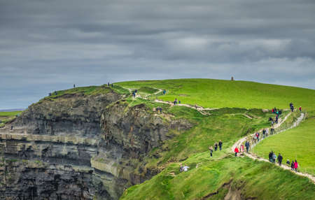 Cliffs of Moher, Ireland -  April 2017 : People walking on a path on top of the Cliffs of Moher on a overcast, cloudy and gloomy day, Irelandのeditorial素材