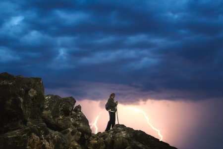 Lonely female trekker admiring mountain view from the top during lightening stormの写真素材