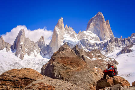 Male trekker resting on the rock in front of the stunning and impressive Mount Fitz Roy near El Chalten in Patagonia, Argentinaの写真素材