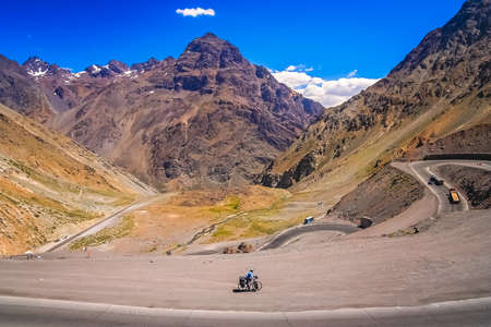 Female cyclist riding downhill on the twisting and turning switchbacks on the beautiful road through high Andes from Artgentina to Chile, South Americaの写真素材