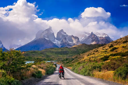Girl standing with her bicycle on the road leading to the impressive Cuernos del Paine peaks in Torres del Paine National Park, Chile, South Americaの写真素材