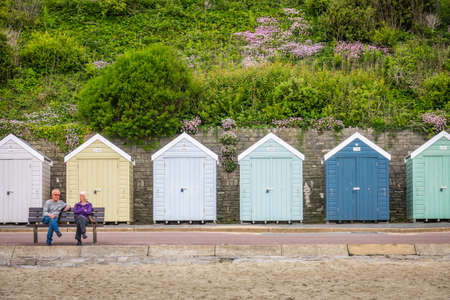 Bournemouth, England - May 29, 2017 : Older couple sitting on the bench in front of the colourful beach huts in Bournemouth, Dorset, Englandのeditorial素材
