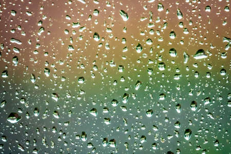 Raindrops on the home window surface against colorful green and yellow backgroundの写真素材