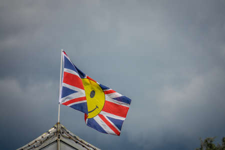British flag with yellow smiley face fluttering in a strong wind on a dark cloudy and rainy day, UKの写真素材