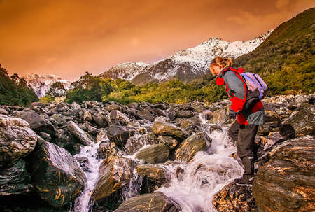 Female trekker crossing the mountain river in the Franz Joseph glacier area in South Island, New Zealandの写真素材