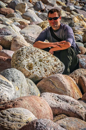 Young man sitting on large boulders on the coastline in northern New Zealandの写真素材