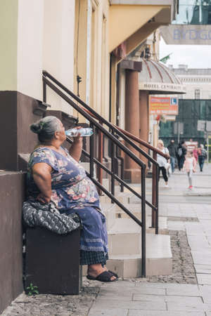 Bydgoszcz, Poland -  August 2017 : Old woman drinking water while sitting in front of an old tenement houseのeditorial素材