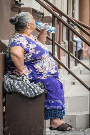 Bydgoszcz, Poland -  August 2017 : Old woman drinking water while sitting in front of an old tenement houseのeditorial素材