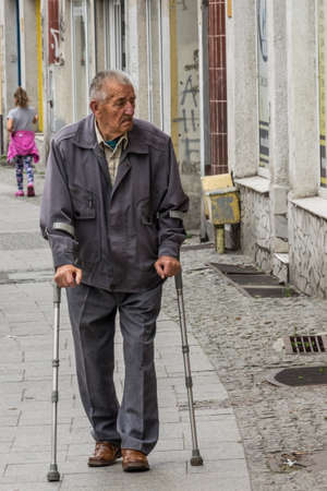 Bydgoszcz, Poland -  August 2017 : Old disabled man walking with crutches on the street in townのeditorial素材
