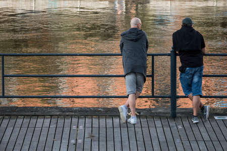 Bydgoszcz, Poland -  August 2017 : Two men standing rested on a metal barrier and looking at a slowly flowing river Brdaのeditorial素材