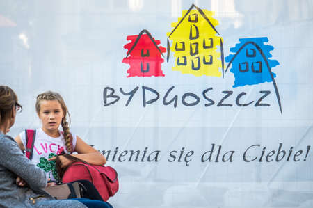 Bydgoszcz, Poland -  August 2017 : Mother and daughter sitting on a bench in front of a canvas with the logo of Bydgoszcz cityのeditorial素材