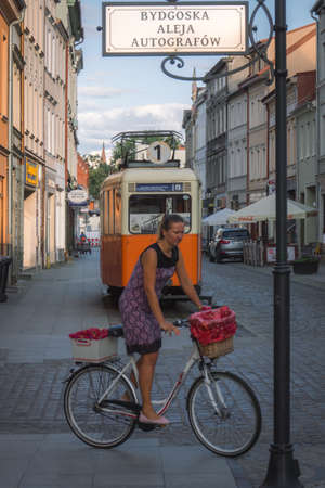 Bydgoszcz, Poland -  August 2017 : Woman cycling on her retro style bicycle with baskets in front of an old, disused, antique tram on the Dluga streetのeditorial素材