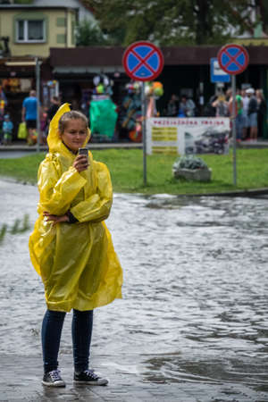 Sarbinowo, Poland -  August 2017 : Girl dresses in yellow raincoat calling for help on her mobile phone after extremely heavy rainfallのeditorial素材