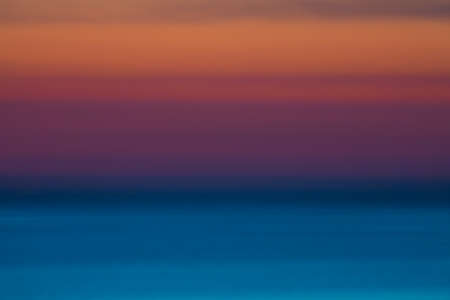 Intentionally blurred and defocused horizontal picture of clouds in the sky above calm sea surface during sunsetの写真素材