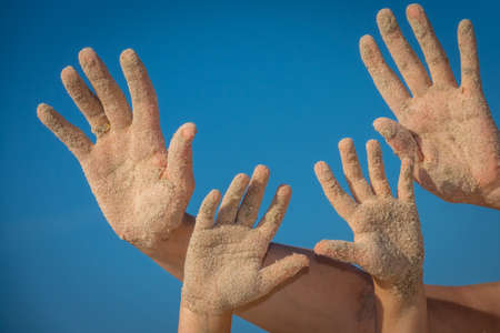 Close up of a  sand covered hands of mother and daughter with blue sky backgroundの写真素材