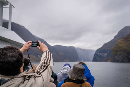 Flam, Norway -  October 2017 :  Tourist taking pictures of beautiful fjords on his mobile during Norway in a nutshell sightseeing cruise through the Aurlandsfjord and  narrow Naeroyfjordのeditorial素材