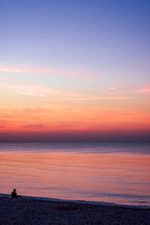 Unidentified lonely man sitting on the sea beach in summer at sunsetの写真素材