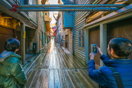 Bergen, Norway -  October 2017 : Asian looking tourists taking pictures of the historic colorful wooden buildings in the old town of Bergenのeditorial素材