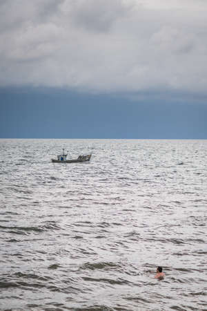 Sarbinowo, Poland -  August 2017 :  Man swimming far from the shore with the stormy skies above and fisherman boat in the distanceのeditorial素材