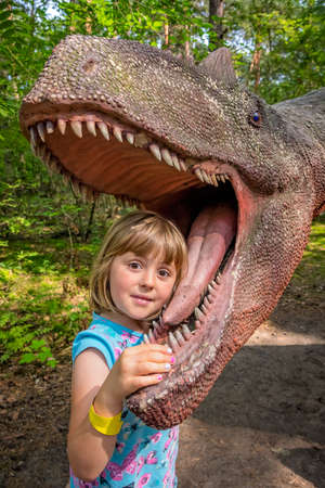 Cute little caucasian girls head in the mouth of a dinosaur replica in an amusement parkの写真素材