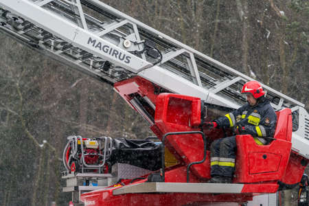 Karpacz, Poland -  February 2018 : Firefighter sitting in control chair operating an extendable crane arm with his colleagues in it cutting branches of a tree after heavy snowfallのeditorial素材