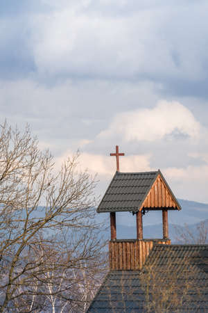 Cross on a wooden rooftop of a building opposite the tower of the catholic church of the Parafia Nawiedzenia NMP in Karpacz, Polandの写真素材